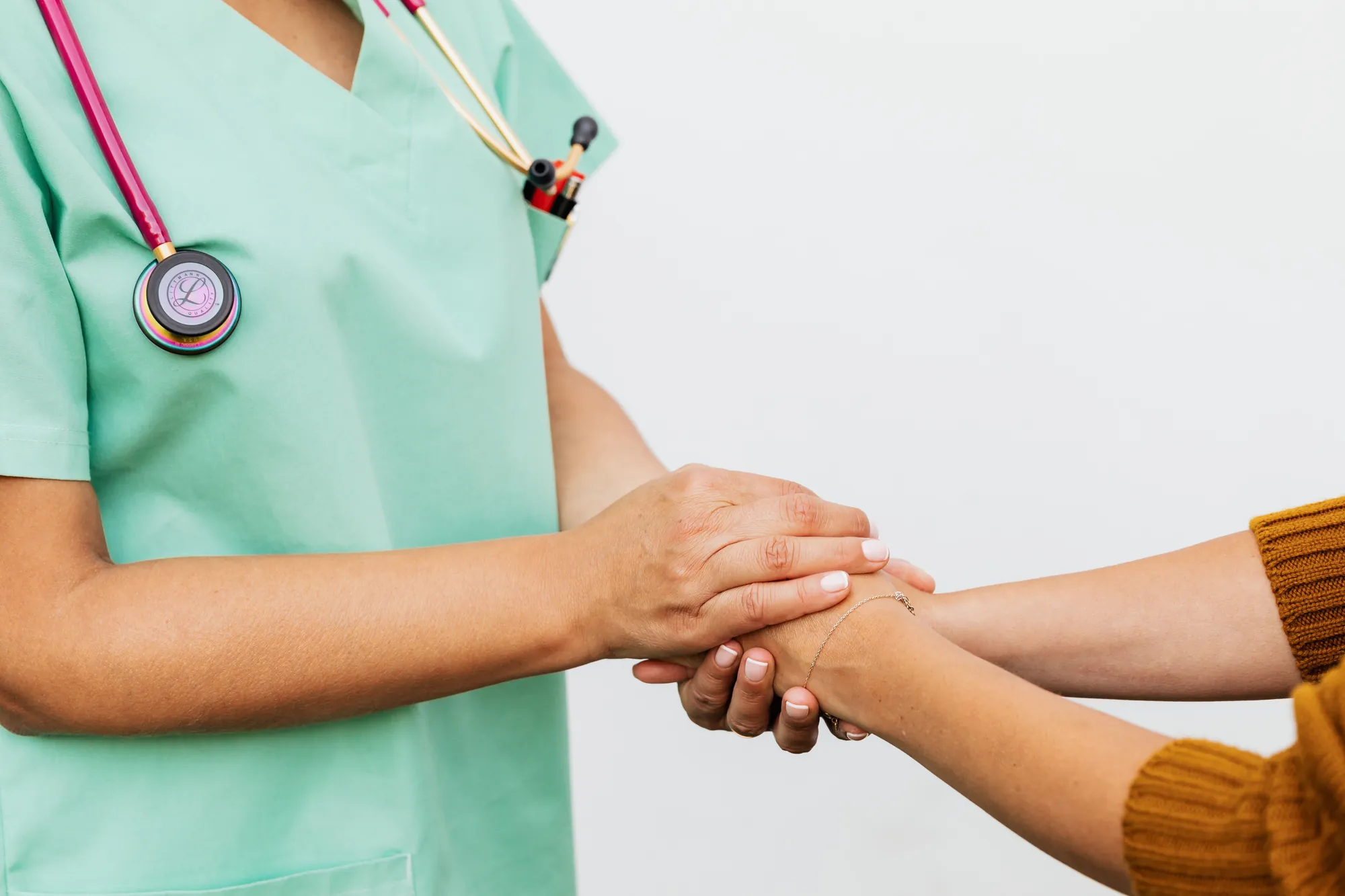 A clinician in scrubs holding a patient's hand in a supportive gesture